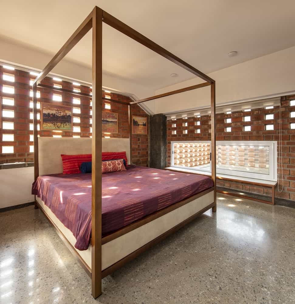 The bedroom has a large wooden four-poster bed that has dark red sheets to pair with the surrounding patterned red brick walls.