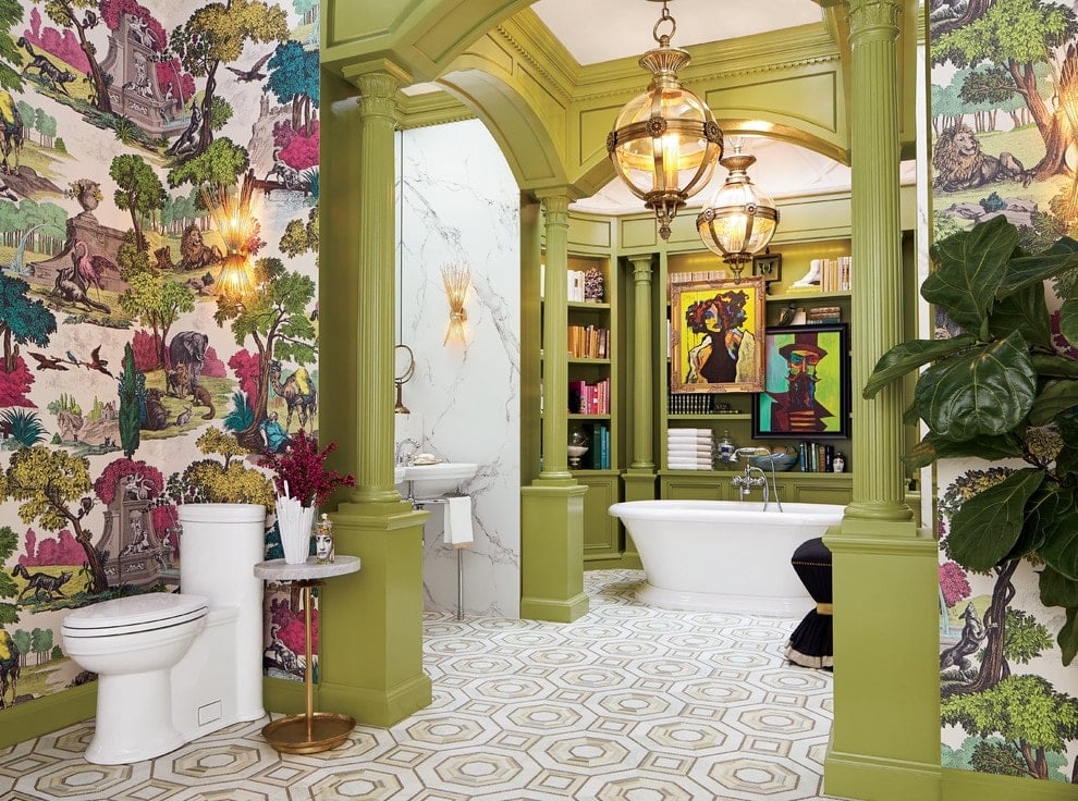 This primary bathroom showcases a combination of olive green walls and wildlife wallpaper providing a gorgeous backdrop to the potted plant and toilet. It has a wash area and a freestanding tub against the built-in shelving lighted by spherical glass pendants.