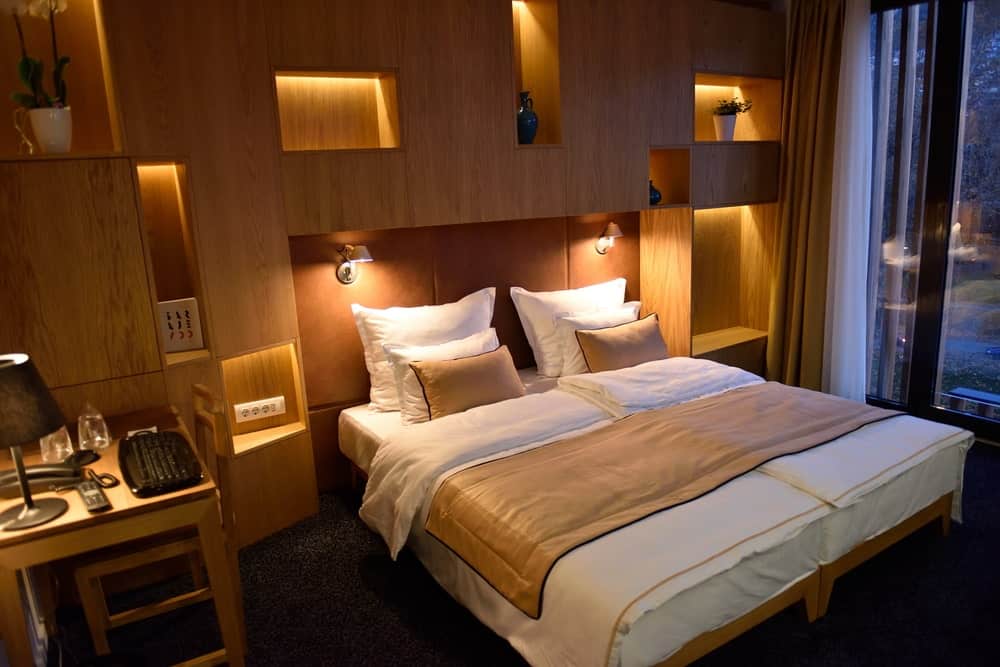 A focused shot at this primary bedroom's large bed lighted by wall lights. The room has brown walls with built-in shelving.