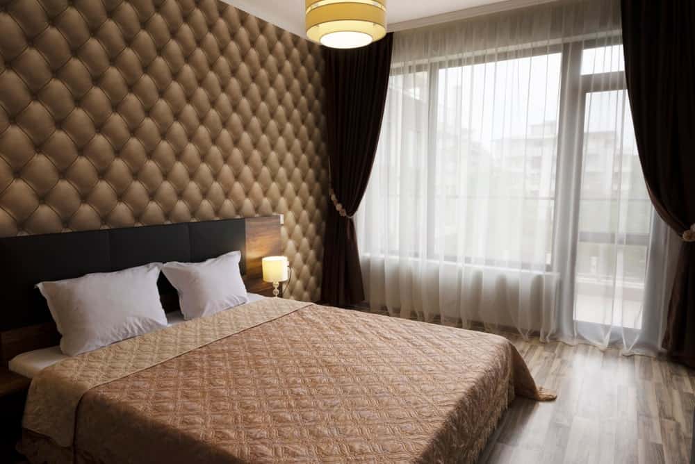 Primary bedroom boasting a luxurious wall and a classy bed. The room offers lovely window curtains and stylish hardwood flooring.