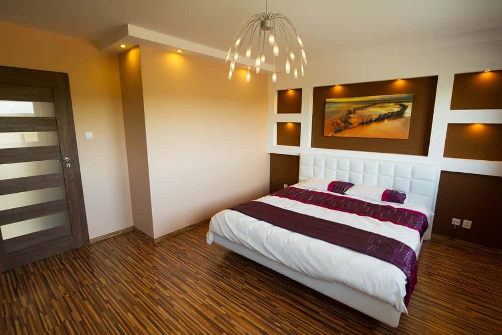 Primary bedroom with stylish flooring and a regular ceiling lighted by magnificent ceiling lighting. The room offers a lovely white bed with a stylish wall behind.