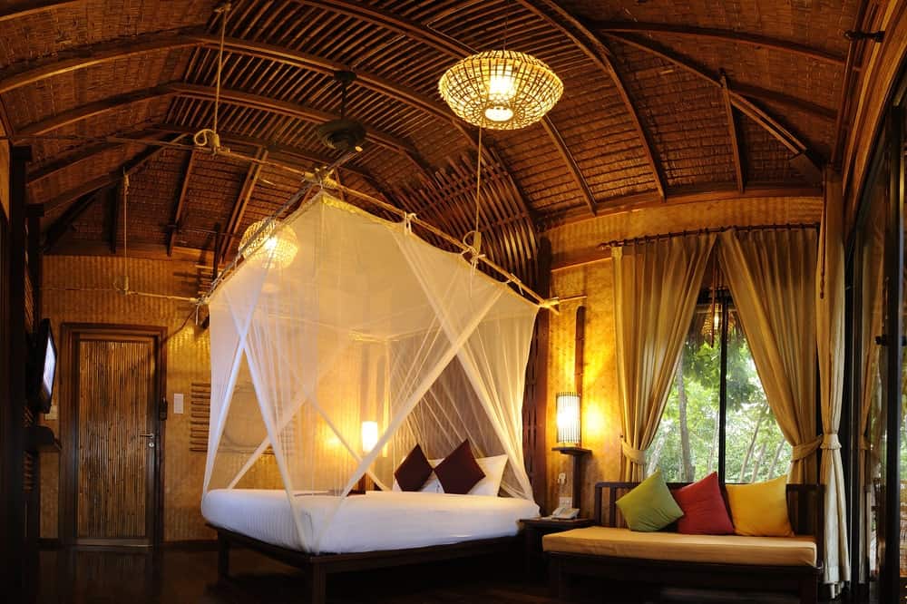 A large primary bedroom boasting a stunning wooden ceiling with beams. The room has a lovely bed set and a simple couch on the side.