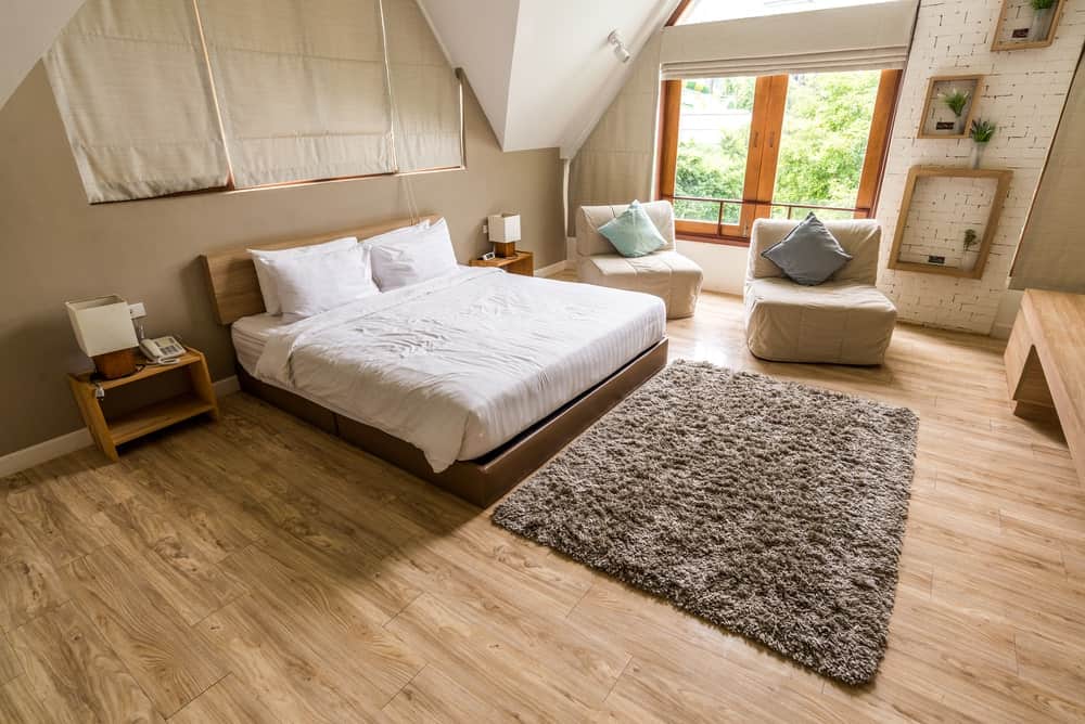 A spacious primary bedroom featuring hardwood floors and brown walls, along with a custom ceiling. The room offers a large cozy bed.