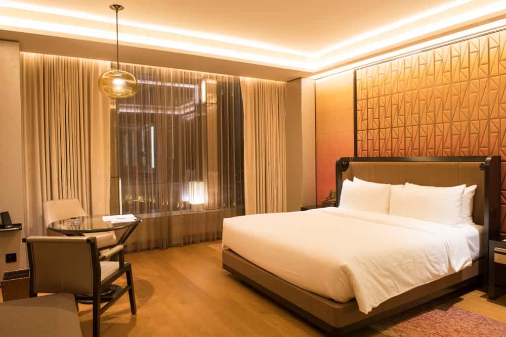Primary bedroom featuring a stylish wall behind the large modish bed. There's a coffee table set on the side lighted by a pendant light.
