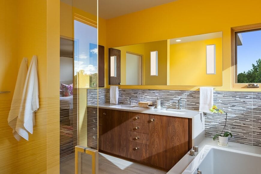 Linear black and white backsplash sets a striking backdrop to the drop-in tub and wooden vanity with a mirrored medicine cabinet on top. It faces the walk-in shower enclosed in a frameless glass panel.
