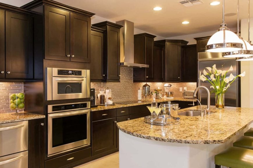The L-shape layout of this elegant kitchen is paired with a beige countertop and backsplash that is augmented by the cabinet lighting. This goes quite well with the dark and classic cabinetry complemented by the stainless steel handles and appliances.