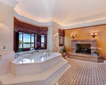 Spacious custom master bathroom with stylish tile flooring, a fireplace, and a drop-in tub on a platform by the windows.