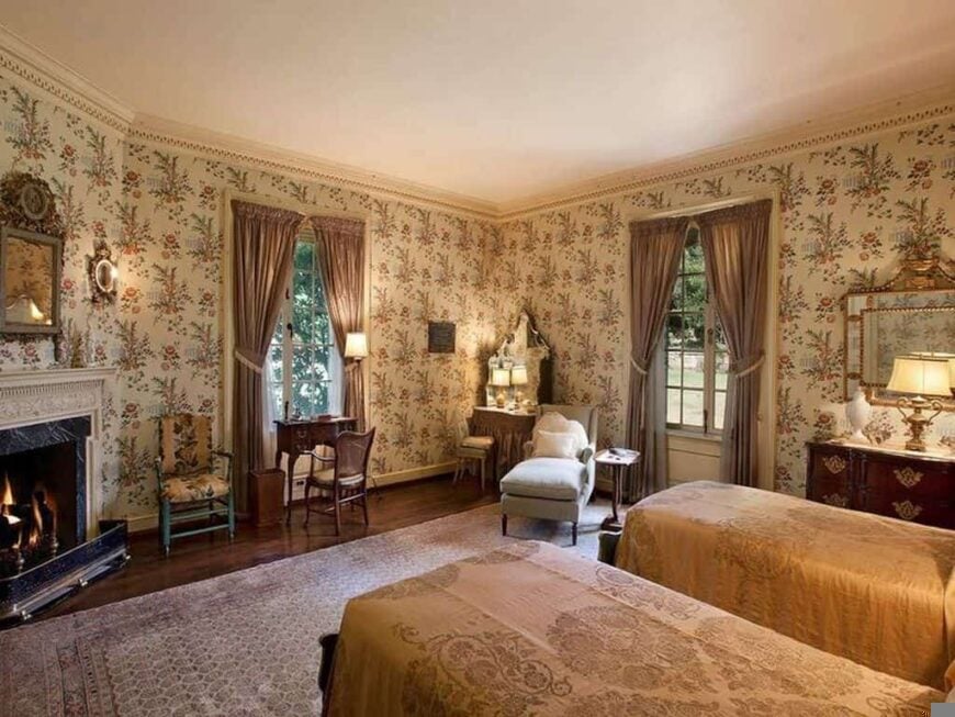 This primary bedroom boasts beautifully decorated walls, along with hardwood flooring topped by a large area rug. There's a twin bed and a corner fireplace as well.
