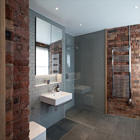 Red brick walls add texture in this gray bathroom showcasing a small shower area and a wall-mounted sink paired with a mirrored medicine cabinet that's fixed against the inset wall.