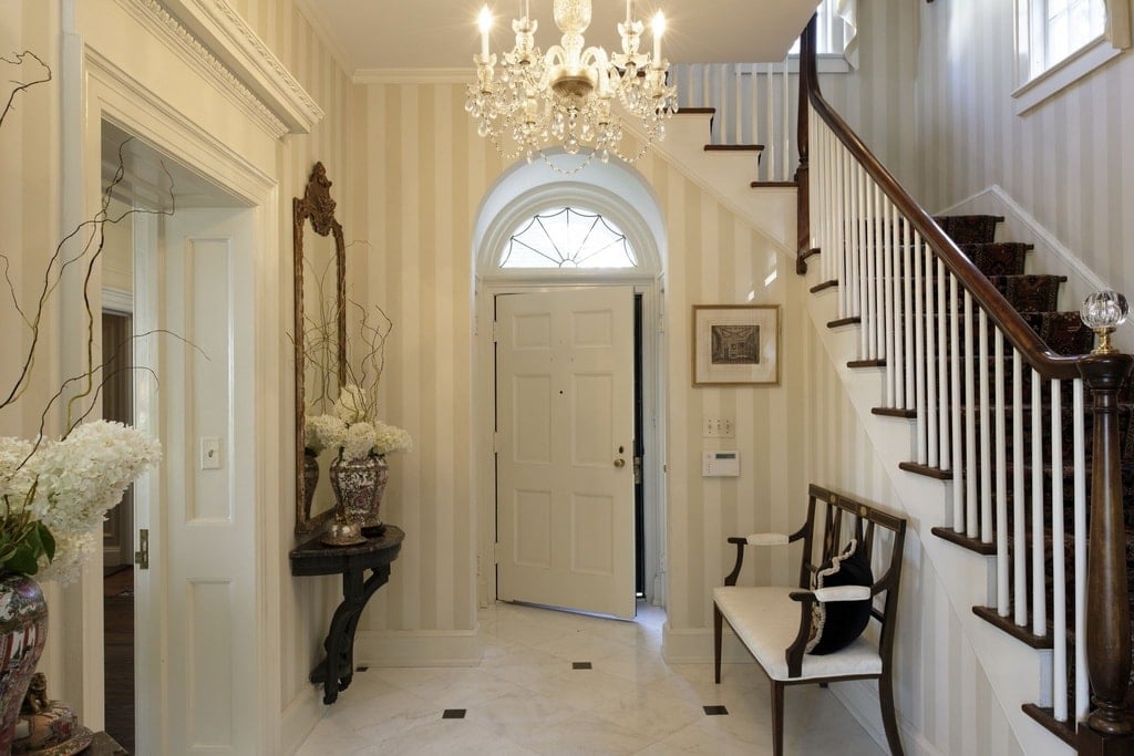 Entry foyer with elegant walls and tiles flooring, lighted by a gorgeous chandelier.