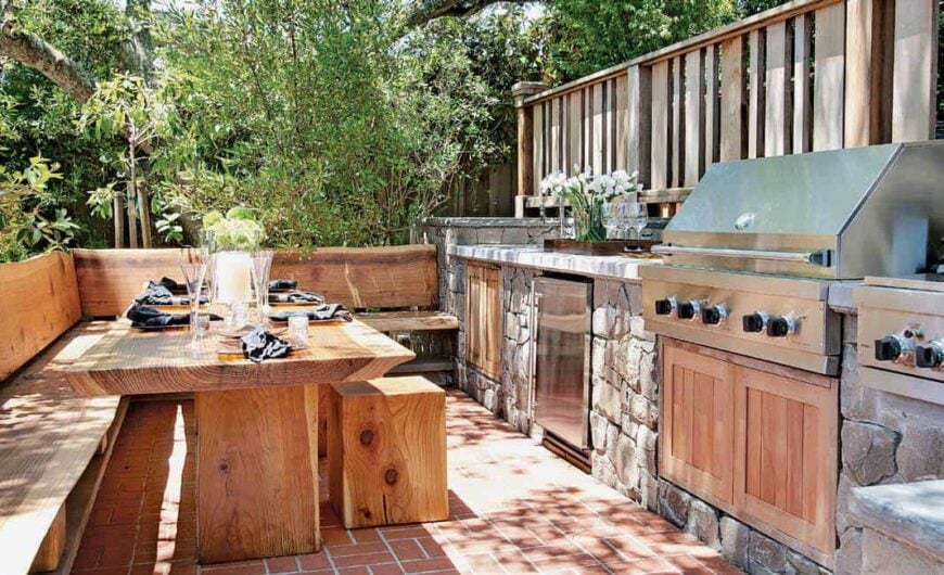 This is a cozy outdoor kitchen with a dining nook of bare wooden dining table, built-in L-shaped bench and small stools that go quite well with the terracotta flooring. This also complements the textured stone structure that houses the stainless steel appliances.