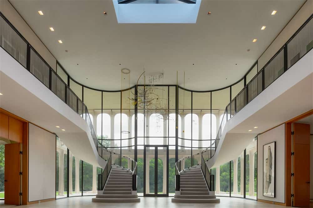 Upon entry of the mansion, you are welcomed by this spacious grand foyer with a high ceiling paired with tall glass walls and glass railings for the indoor balcony.