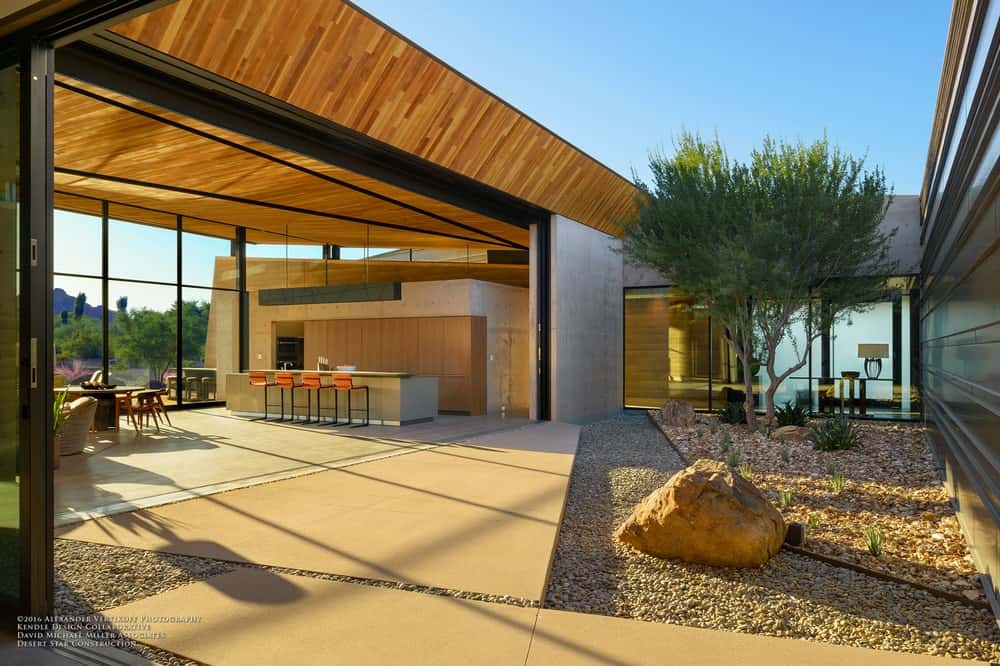 A look at this home's kitchen from the outdoor area. The area boasts a stunning tall ceiling and has glass window walls on the side.
