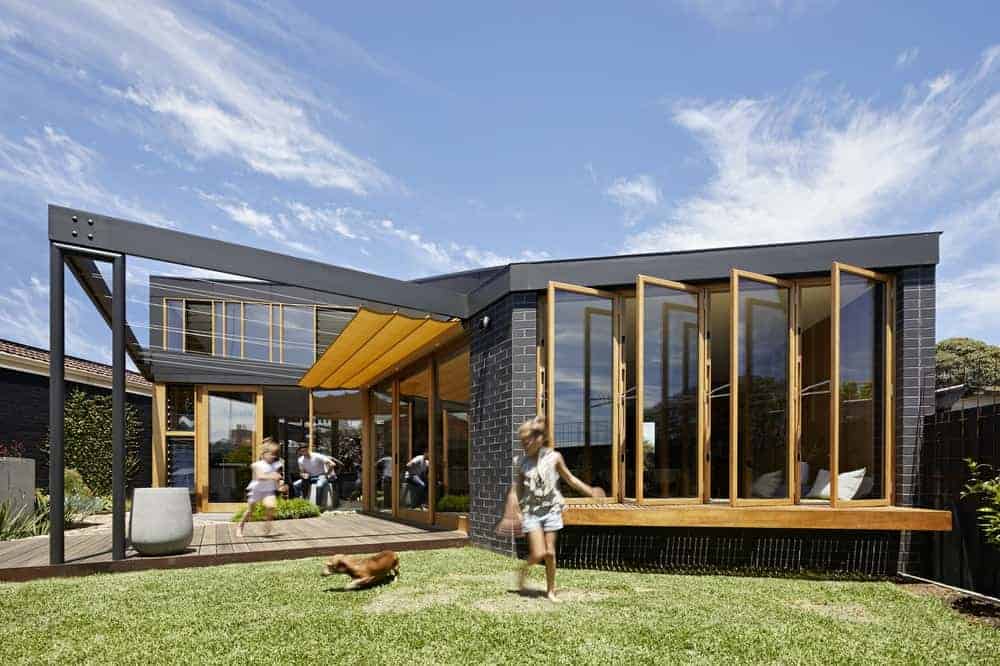 A fancy house finished in black, designed by BENT Architecture. It's a stylish contemporary house with glass windows and doors. The lawn area is just perfect for kids and pets.