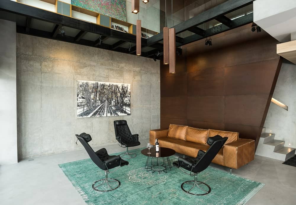 This is a stylish living room with a large brown leather sofa on the far side by the large brown wall paired with black leather loungers and a small coffee table topped with decorative lighting.