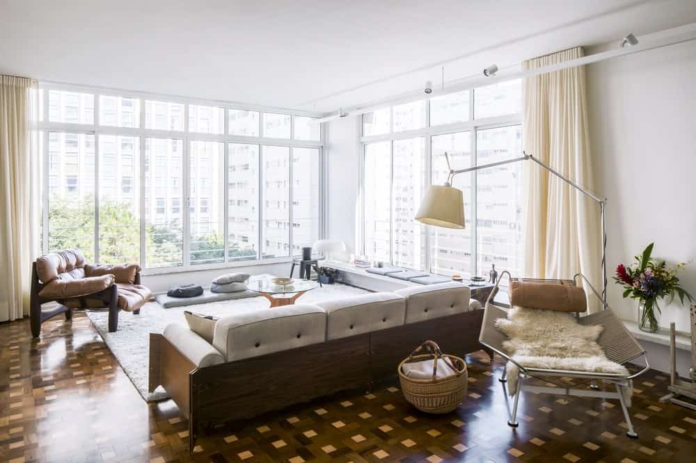 This view of the living room showcases more of the glass walls that bring in natural lighting for the sofas and coffee table and to contrast the dark tone of the patterned flooring.