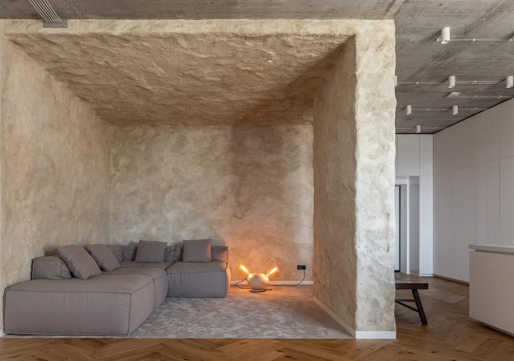 This is a look at the living room that has a large gray L-shaped sectional sofa at a section with textured stone walls and ceiling.