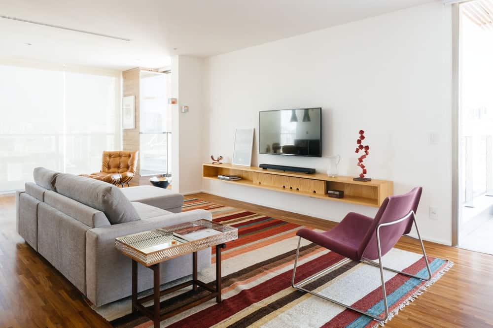 This view of the living room showcases the large gray sofa paired with a colorful patterned area rug across from the floating entertainment shelf of the TV.
