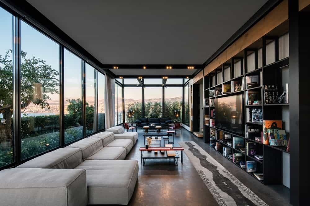 This is the living room with a large gray sectional L-shaped sofa paired with a glass-top coffee table across from the large built-in structure with shelves surrounding the wall-mounted TV.