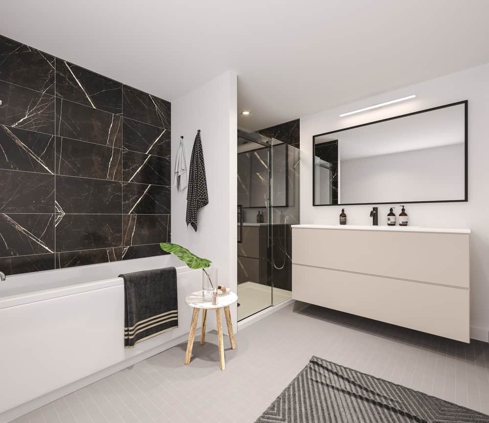 A walk-in shower flanked the floating vanity in this primary bathroom. It also has a corner tub with black tiles walls and a large framed mirror.