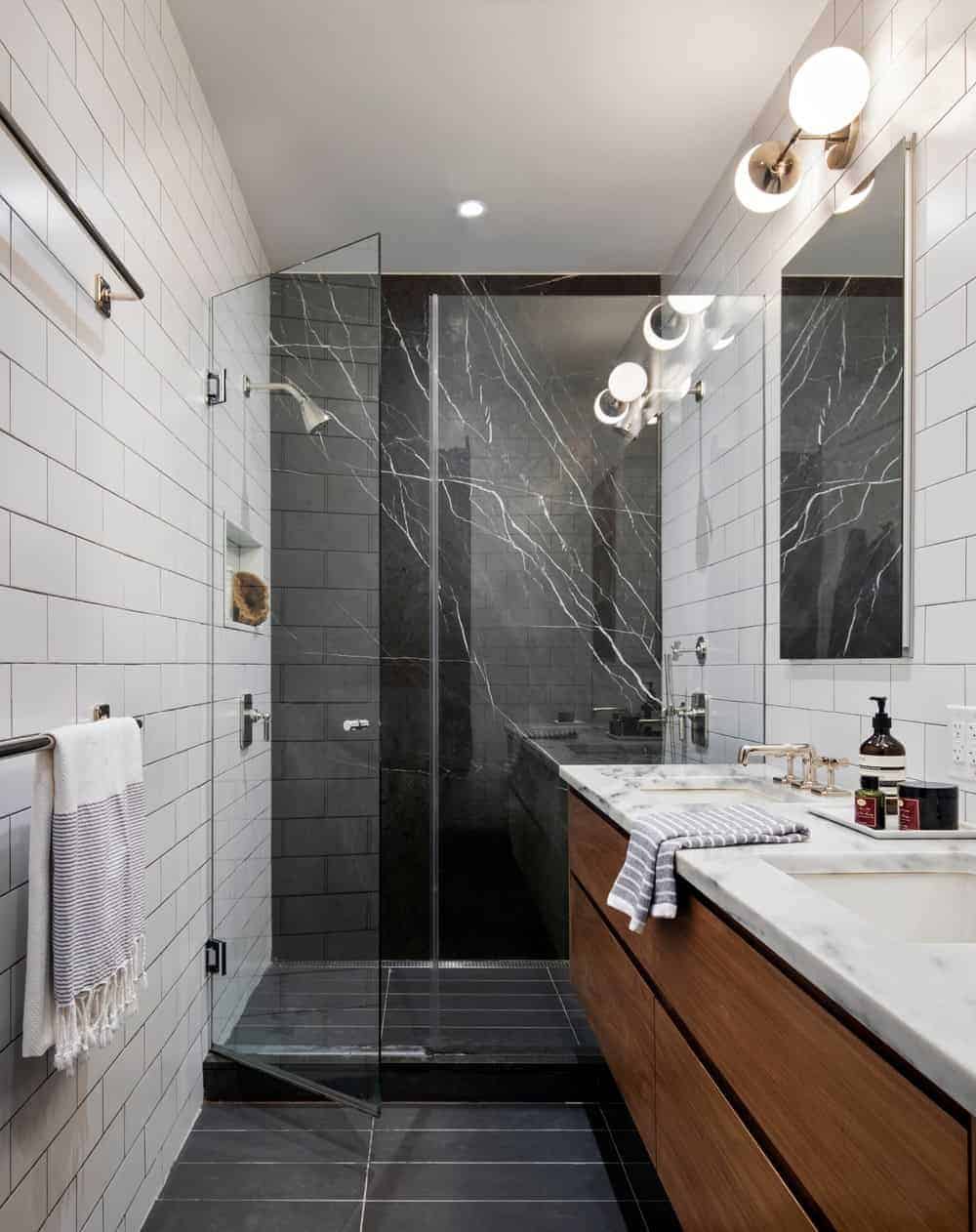 There’s a dual sink vanity on the side fitted with cabinets and a walk-in shower enclosed in the glass door. It also has a black and white tiled wall.