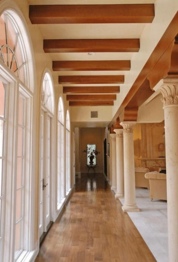 Long hallway with large arched windows, exposed wooden beams, and elegant columns.