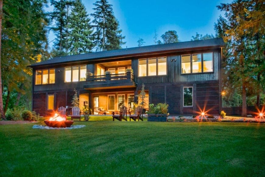 The rear exterior view shows the veranda and covered deck along with plenty of glazed windows flooded by the warm glowing lights.