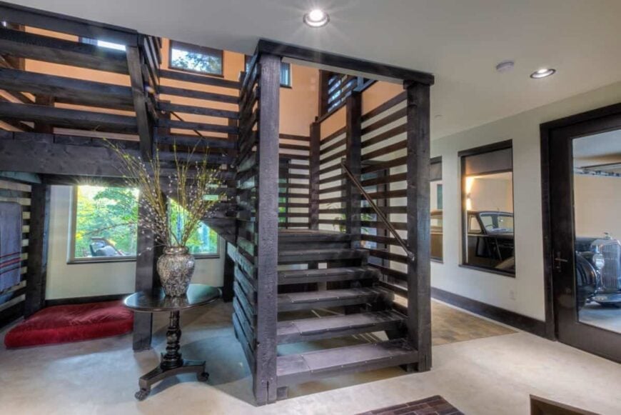 The foyer has a dark wood staircase and a round wooden table topped with an antique vase.