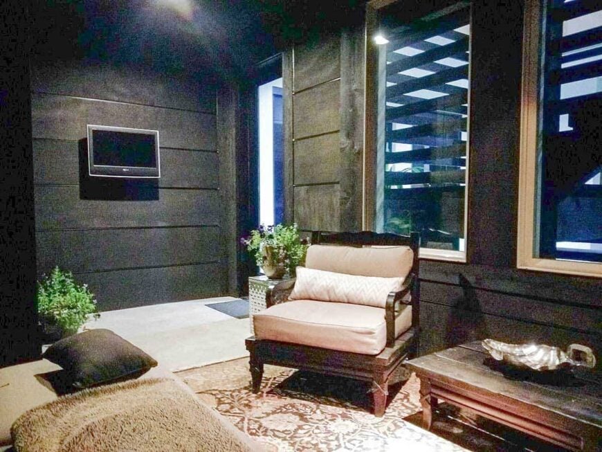 The covered deck offers a wall-mounted TV, a rustic coffee table, and cozy seats over a classic area rug.