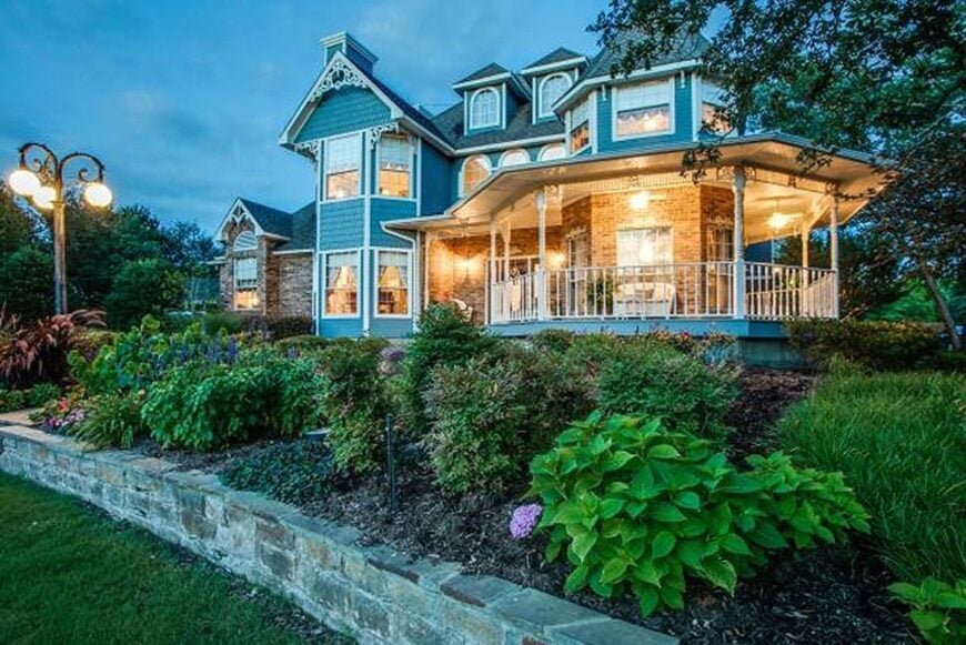 The home's angled side view shows the wrap-around covered porch framed with white railings and exterior columns.