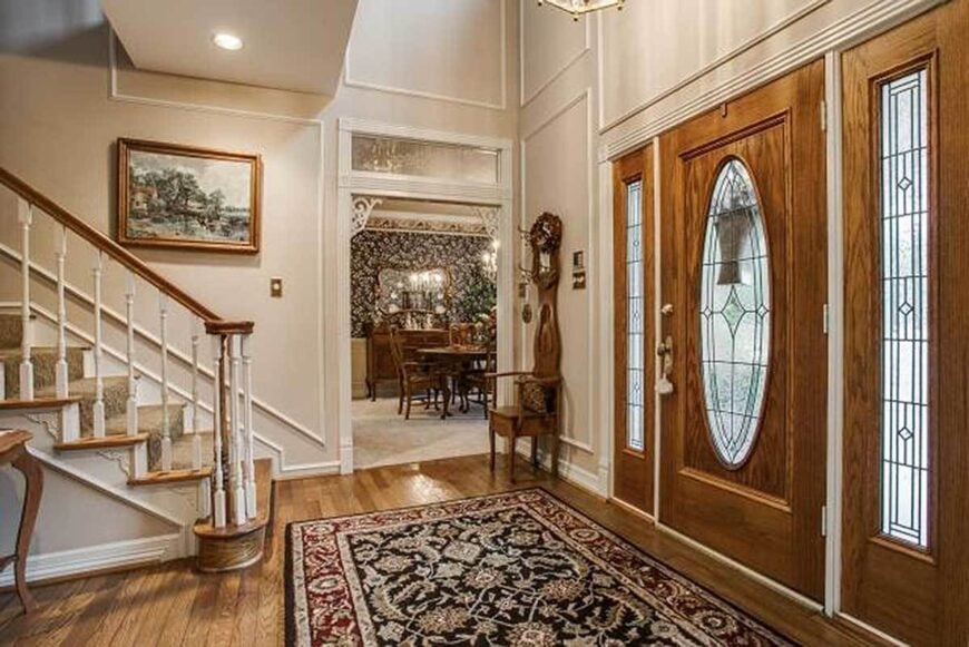 The home's foyer has a wooden front door, a large patterned rug, and a view of the formal dining room.