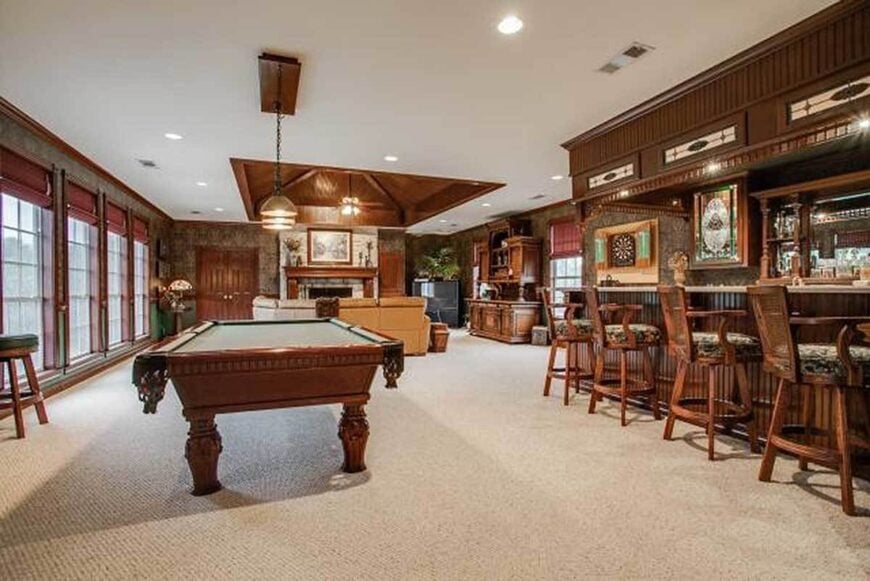 The recreation room is filled with a beige sofa, a billiard table, and a wet bar lined with cushioned counter chairs.
