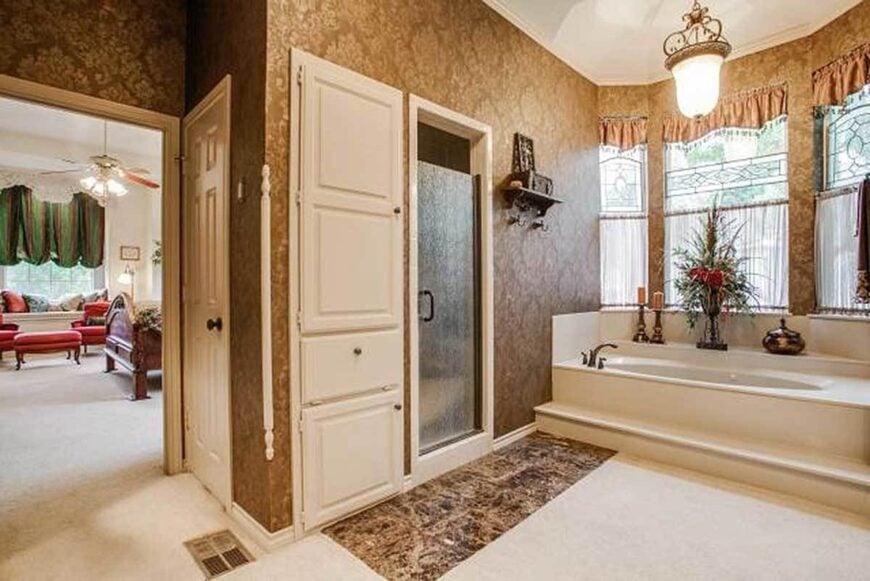 The primary bathroom has a walk-in shower and a deep soaking tub by the bay window lit by a glass pendant.
