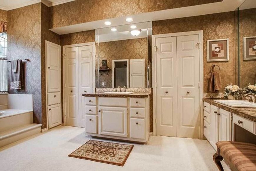 The opposite side view of the primary bathroom shows the two sink vanities accompanied by a floral rug and a striped stool.