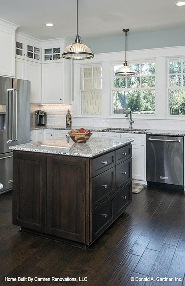 A closer look at the center island shows the dark wood pullouts and granite countertop lit by glass dome pendants.