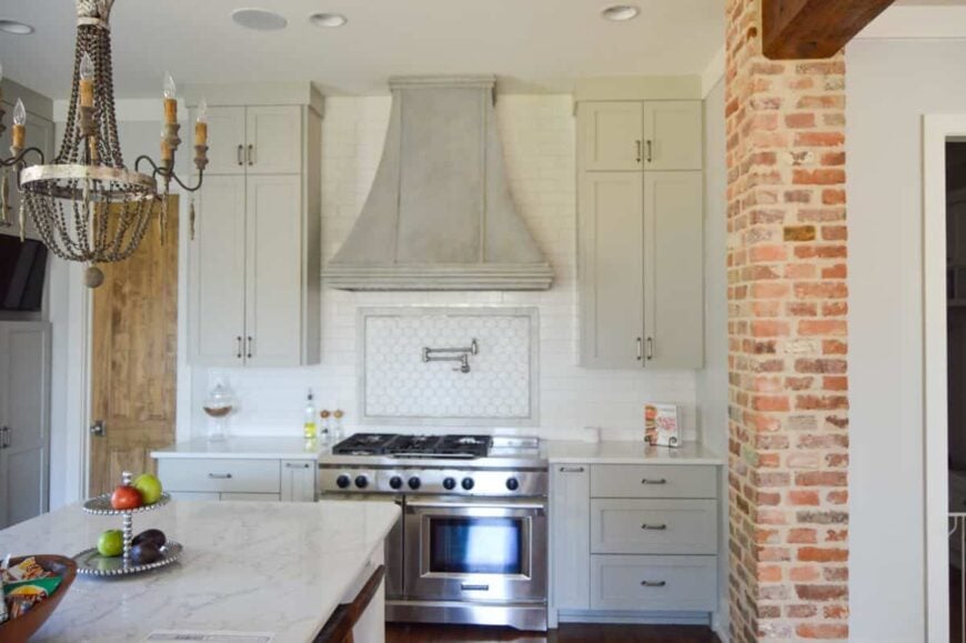 Kitchen with white cabinetry, stainless steel appliances, and a marble top island illuminated by a beaded chandelier.
