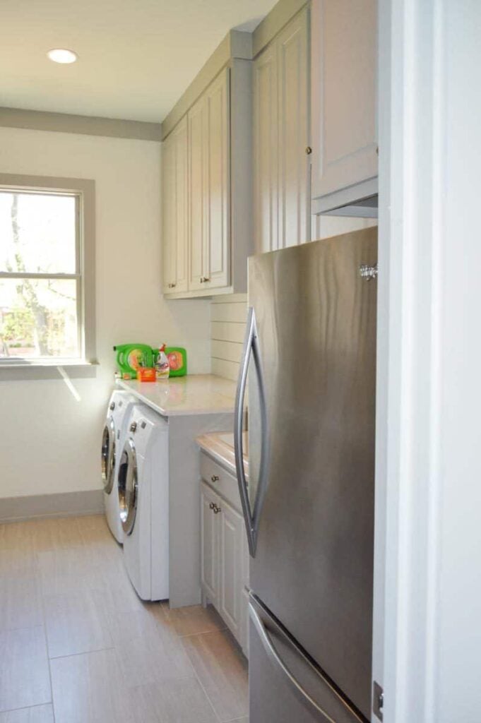 The utility room is equipped with a two-door fridge, white cabinets, and front load washing machine and dryer under the marble countertop.