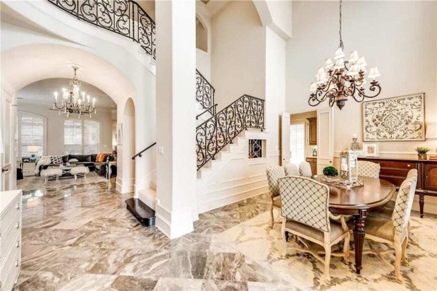 Formal dining room beside the intricate staircase offering a wooden buffet bar and classy dining set under the ornate chandelier.