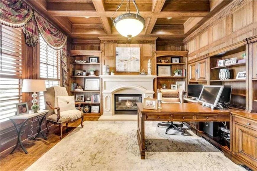 Home study with a fireplace, built-in desk, and wood-paneled walls matching with the coffered ceiling.