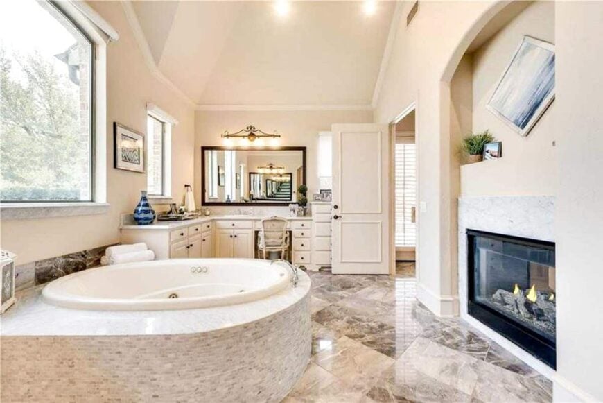 Primary bathroom with curved vanity, a whirlpool tub, and a glass-enclosed fireplace fitted on the arched inset wall.