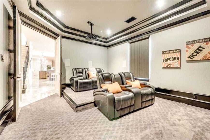 The home theater has a stunning step ceiling and black leather recliners accented with orange pillows.