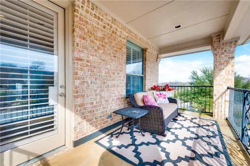 Balcony with wicker cushioned sofa and a metal side table over a large patterned rug.