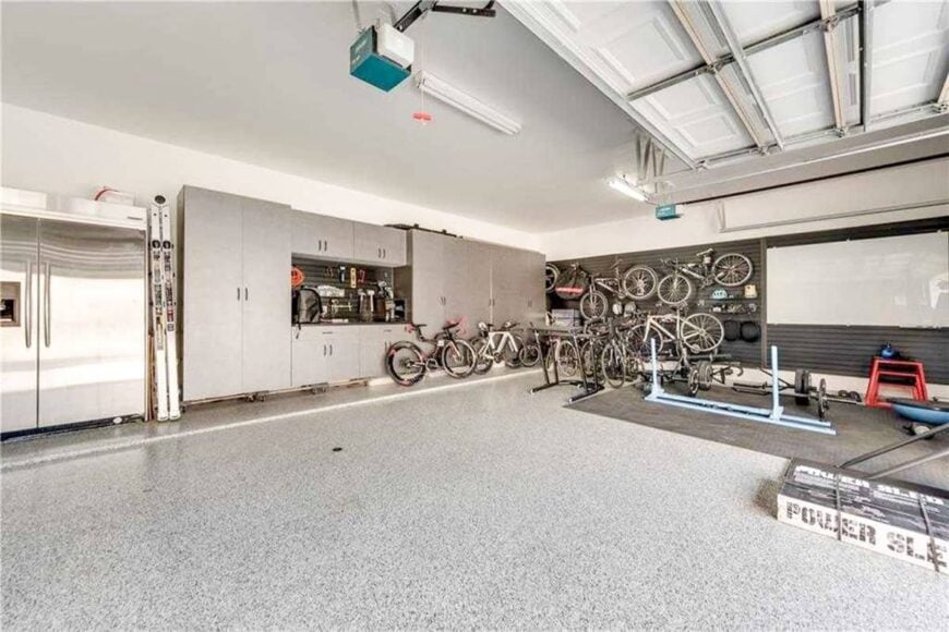 The spacious garage has a two-door fridge, gray cabinets, and lots of bikes gathered in the corner.