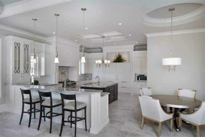 The large kitchen with a breakfast nook offers a two-tier peninsula and a round dining table under a drum pendant light.