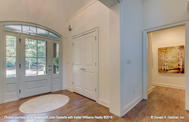 The foyer has a white glazed front door complemented with an oval rug that lays on the hardwood flooring.