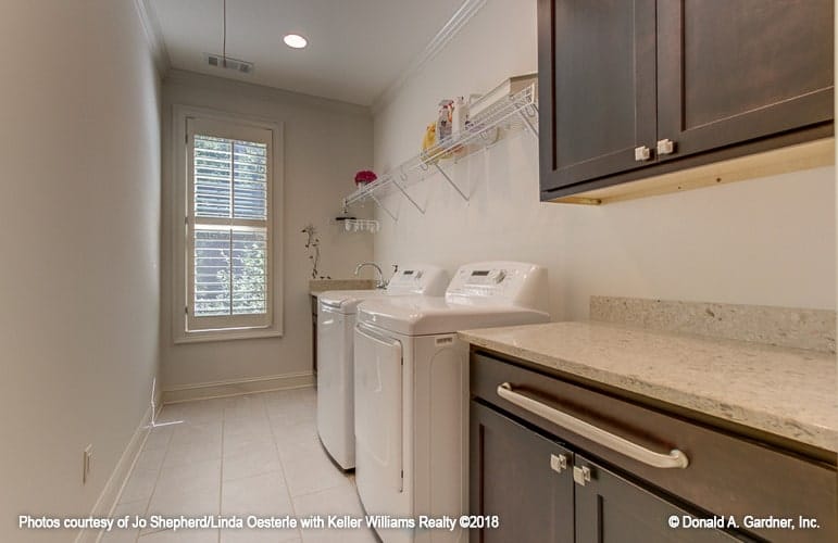 Utility room with dark wood cabinets, granite countertops and top load washing machine and dryer under the white metal rack.
