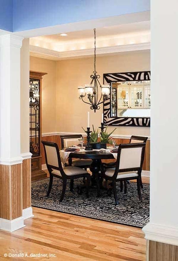 Formal dining room with a glowing tray ceiling and beige walls adorned by a zebra framed mirror and wooden wainscoting.