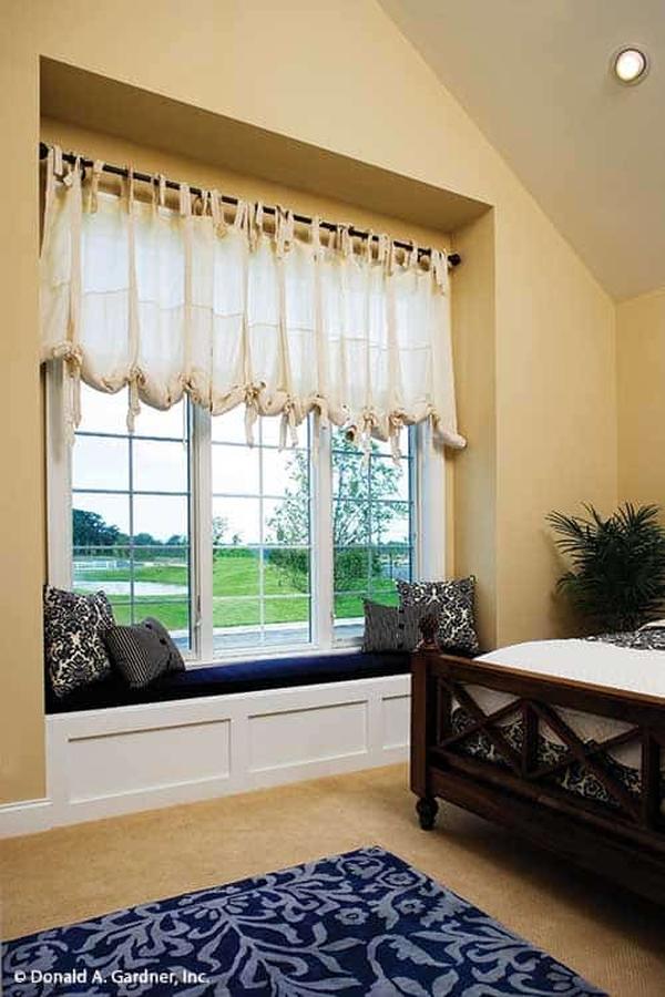 This bedroom features a blue printed rug and a window seat dressed in white sheer curtains.