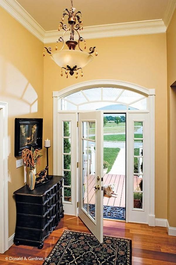 The foyer has a glass front door, black console table and a floral area rug that lays on the polished hardwood flooring.
