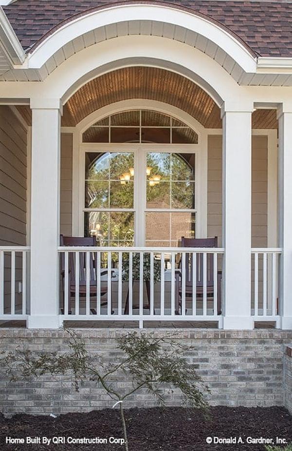 Home's front porch defined with a decorative archway. It is filled with wooden chairs and a matching side table.